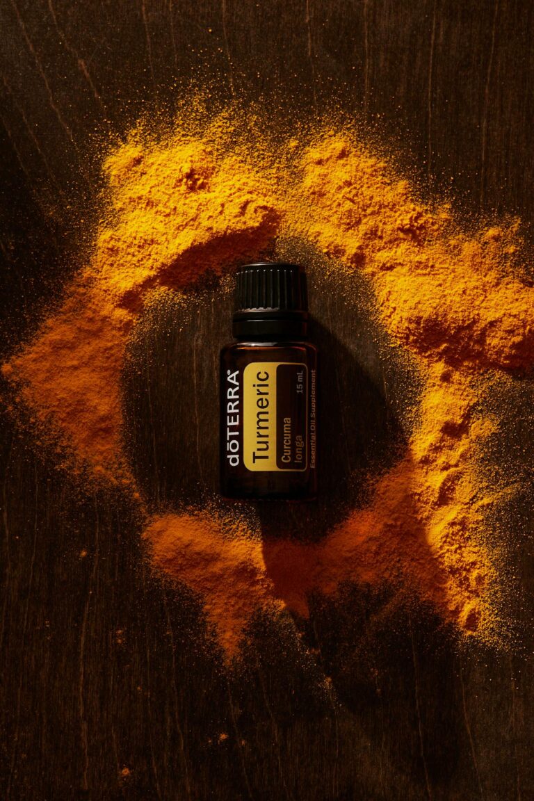 Top view of turmeric essential oil among vibrant powder on a wooden surface.